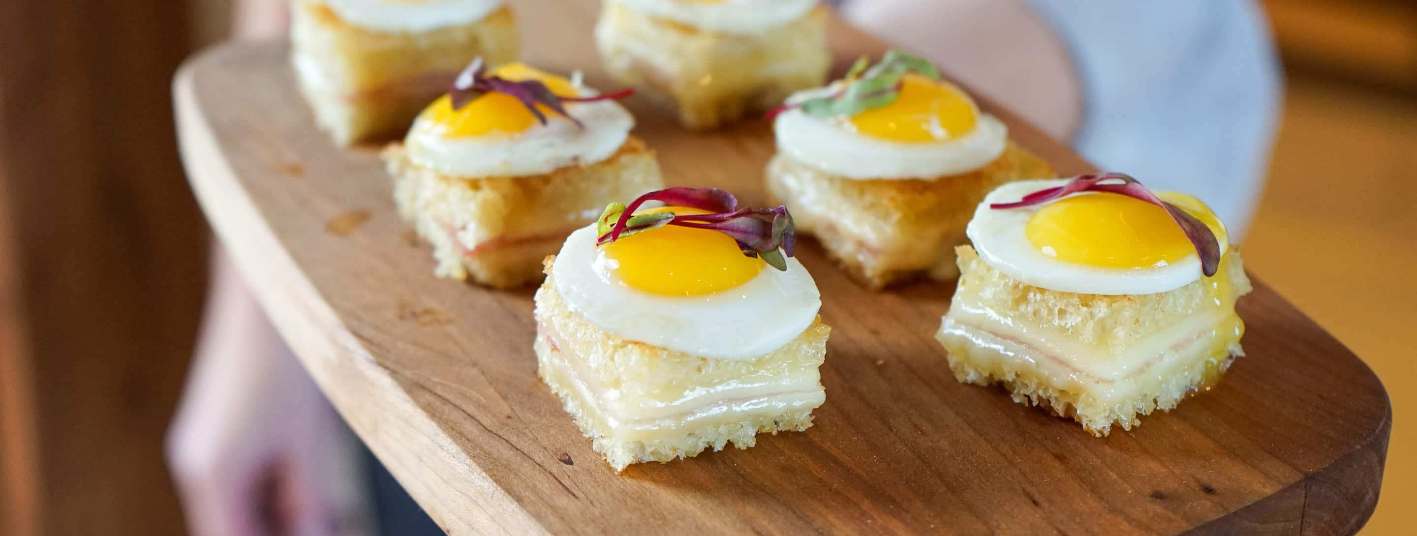 A Bistro Catering server holding a tray of quail egg sandwiches with fresh micro greens at a Jackson Hole, Wyoming event.