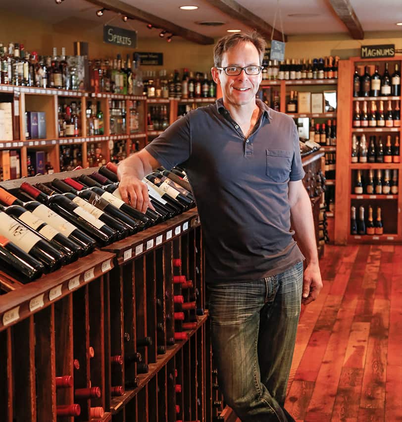 Portrait of Fine Dining Restaurant Group Vice President of Beverage, Neil Loomis, standing next to the wine selection at Bin 22 restaurant in Jackson, Wyoming.